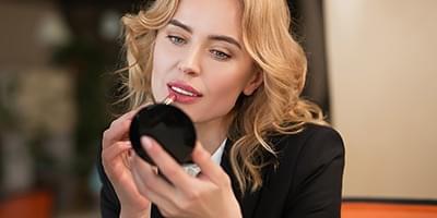 Woman applying lipstick while looking in her compact mirror