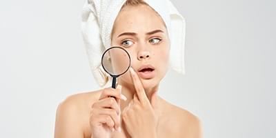 Woman holding magnifying glass looking at acne on face