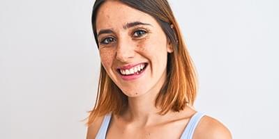 Woman with freckles smiling at camera in tanktop